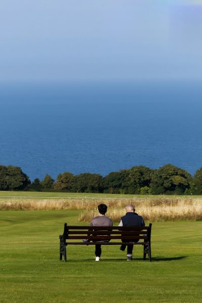 Due persone dialogano seduti su una panchina: come scrivere i dialoghi di un romanzo?